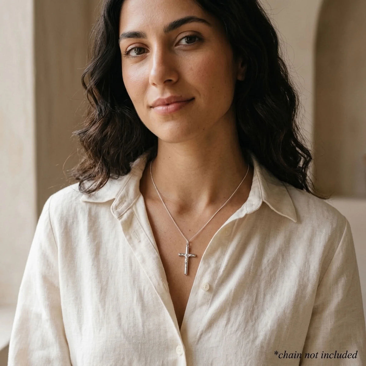 Woman wearing a small mirror-polished sterling silver crucifix pendant with raised Corpus, chain not included.