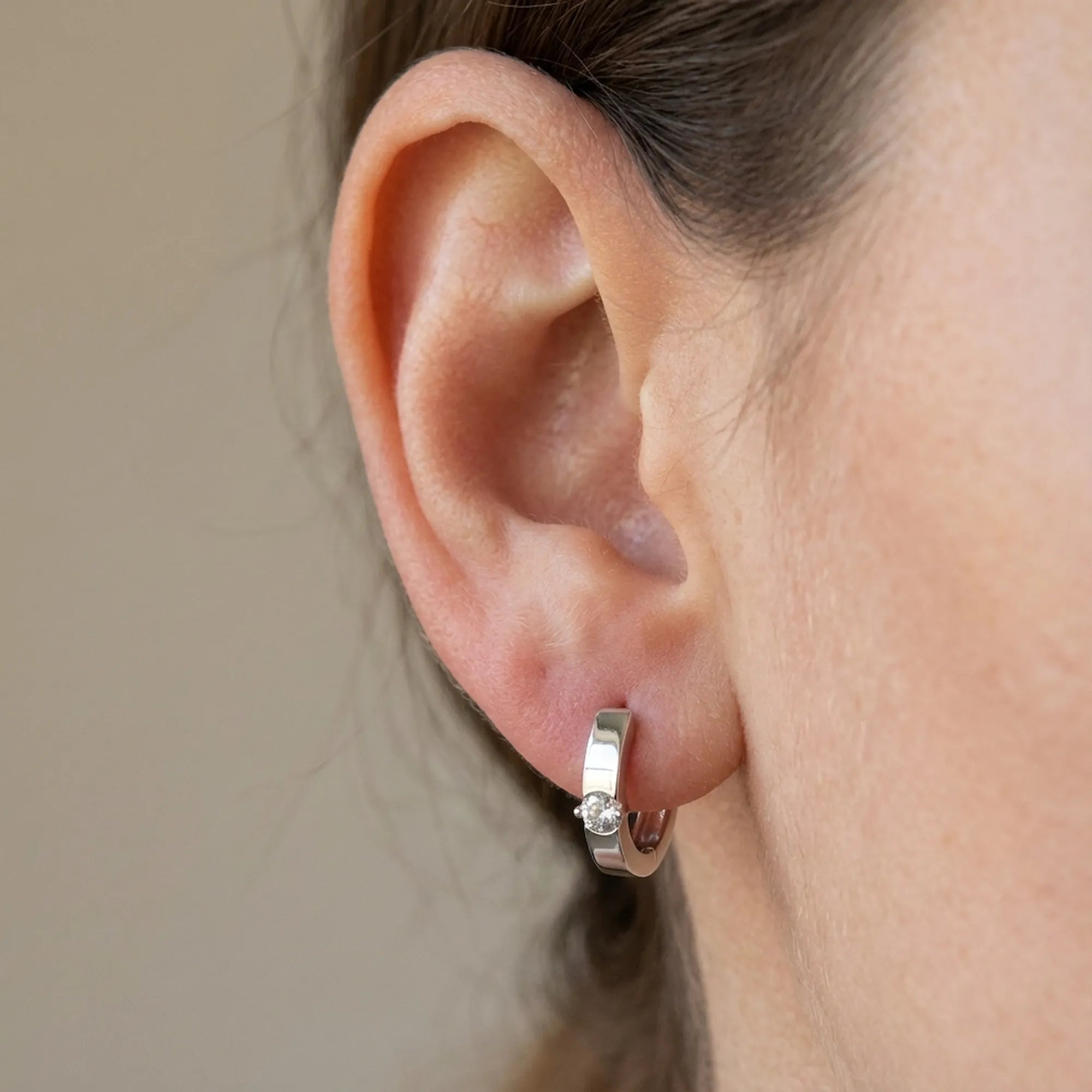 Solitaire Cubic Zirconia huggie earring worn on the ear — slim rhodium 925 sterling silver hoop with a single front stone