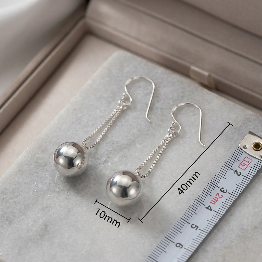 Silver sphere drop earrings with ruler showing 40mm total length and 10mm sphere diameter on grey surface