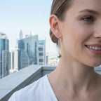 Woman wearing silver sphere drop earrings on rooftop terrace with Business Bay Dubai skyline in background
