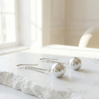 Pair of silver sphere drop earrings laid on white stone surface in bright minimal interior setting UAE.