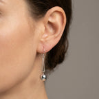 Close-up of ear wearing silver sphere drop earring on double box chain showing polished orb and shepherd hook