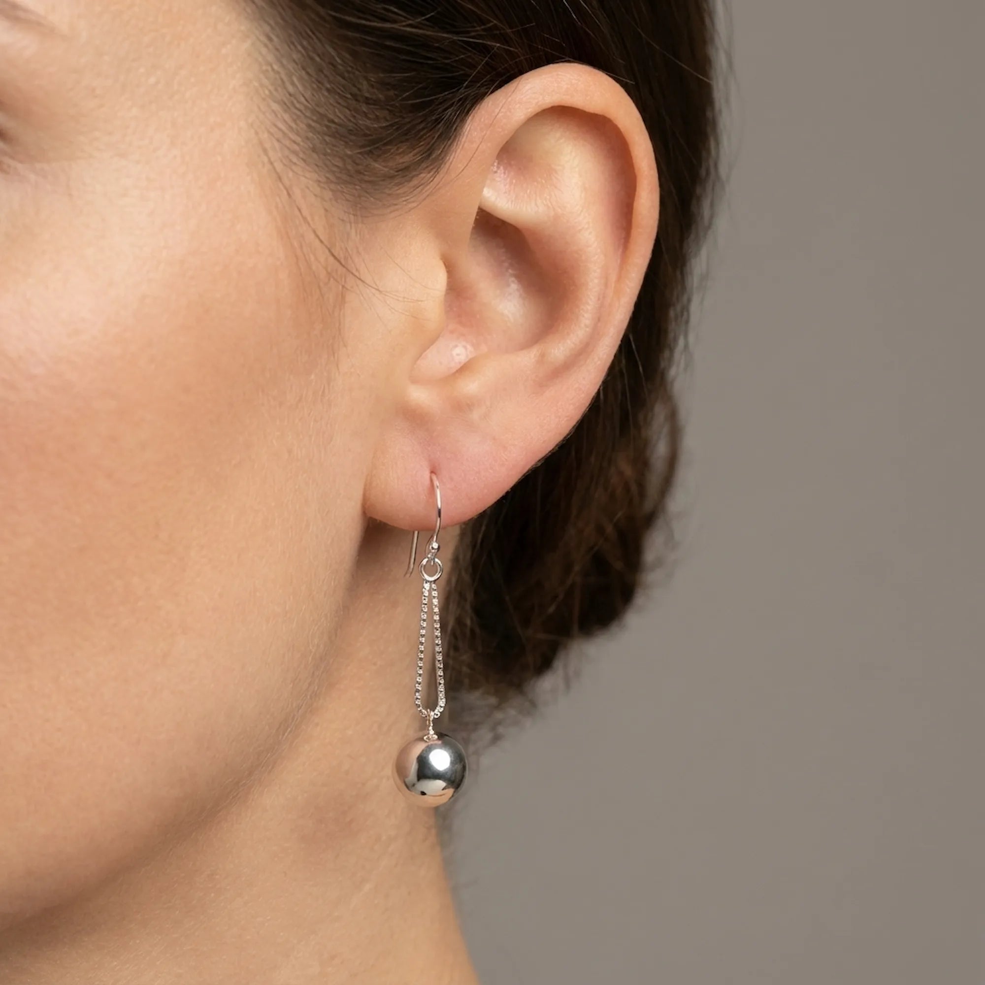 Close-up of ear wearing silver sphere drop earring on double box chain showing polished orb and shepherd hook