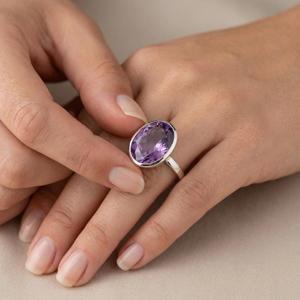 Close up of a woman's hands wearing the 16 by 12 millimeter oval amethyst silver statement ring.
