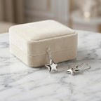 Silver star drop earrings displayed beside a Luna Dura cream velvet gift box on a white marble surface