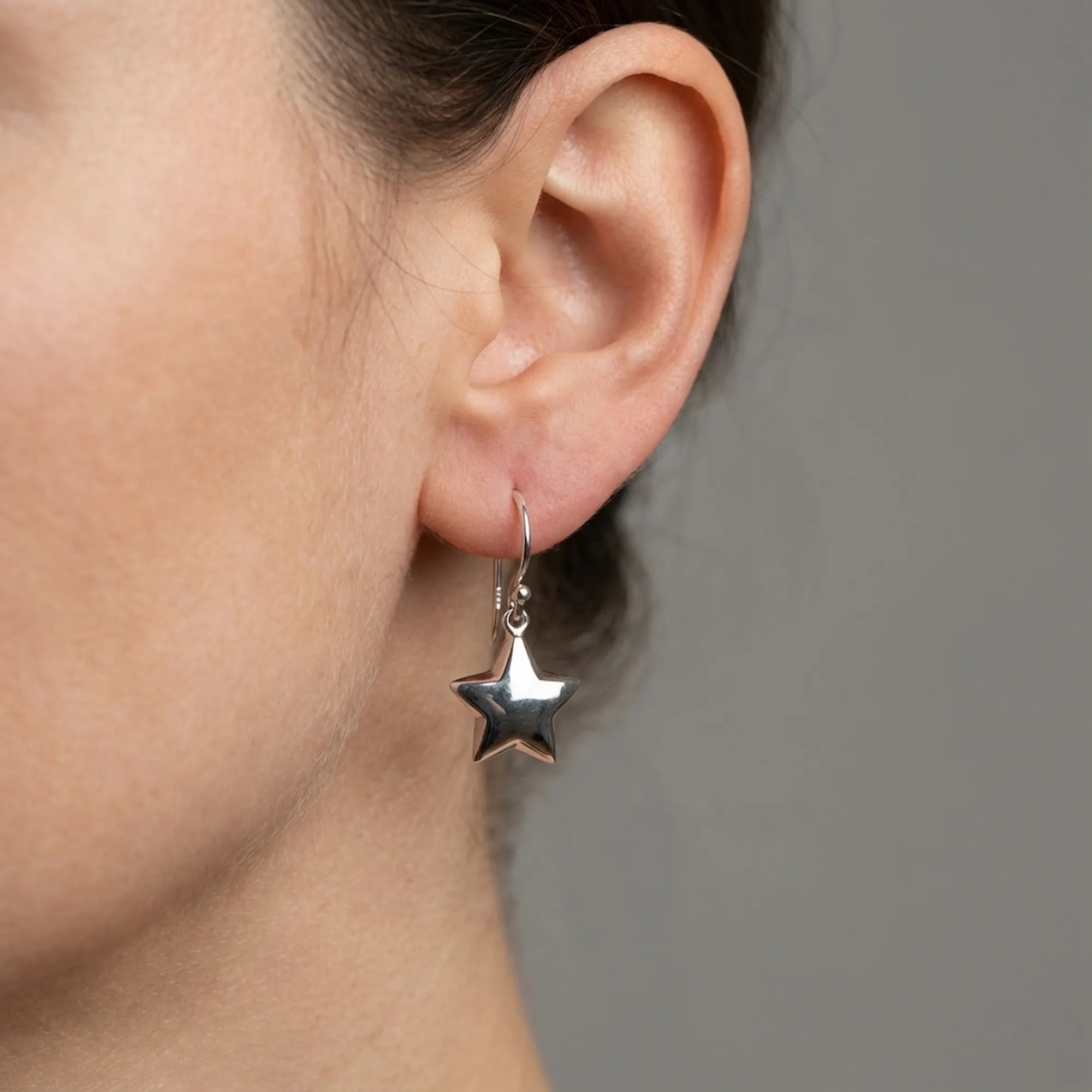 Woman wearing puffed silver star drop earrings on shepherd hook, close-up side profile showing scale and swing