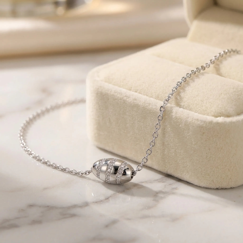 Stardust bead necklace on marble surface beside cream velvet gift box, pavé CZ detail on silver barrel visible