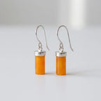 Pair of cylindrical honey orange amber drop earrings with polished sterling silver caps and hooks, isolated on a clean white background