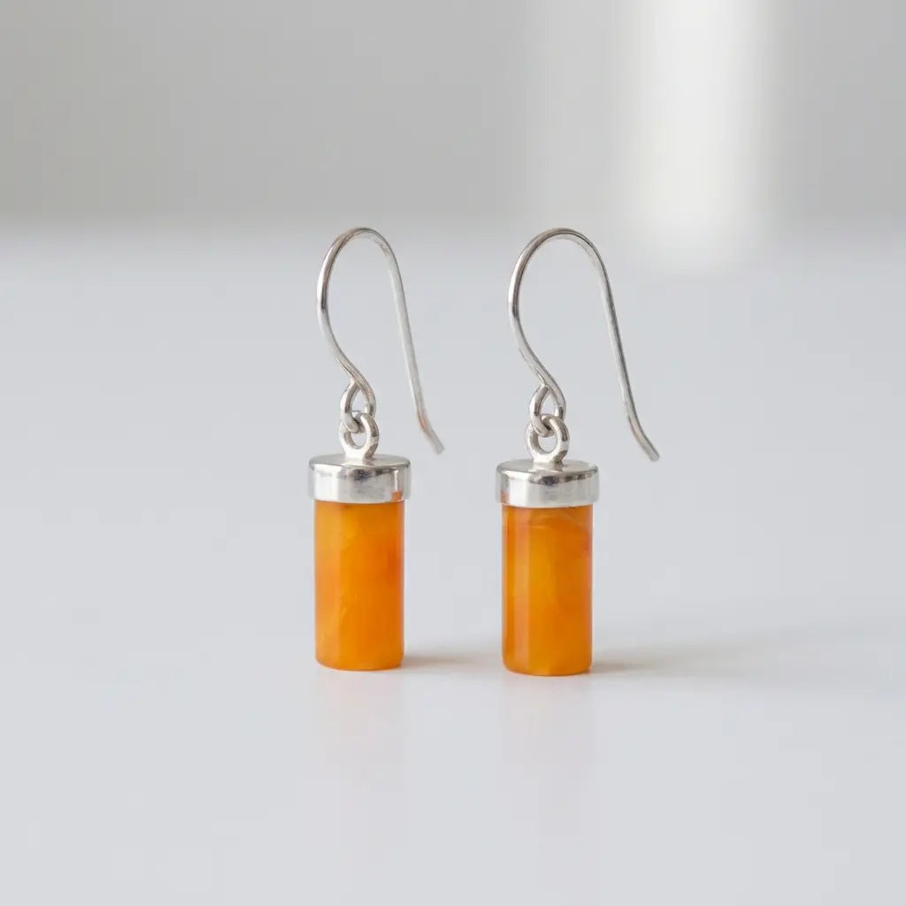 Pair of cylindrical honey orange amber drop earrings with polished sterling silver caps and hooks, isolated on a clean white background