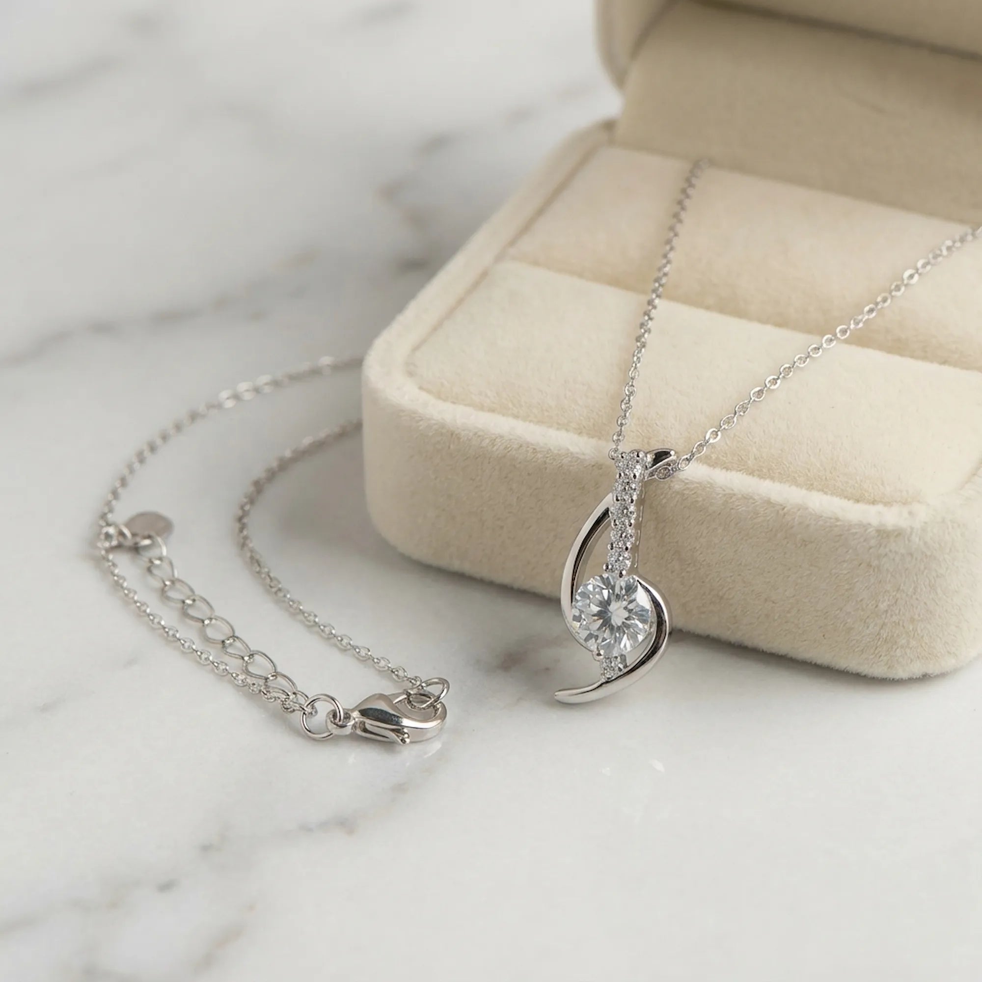 Swirl arc silver pendant necklace on marble beside cream velvet gift box, lobster clasp and extender visible