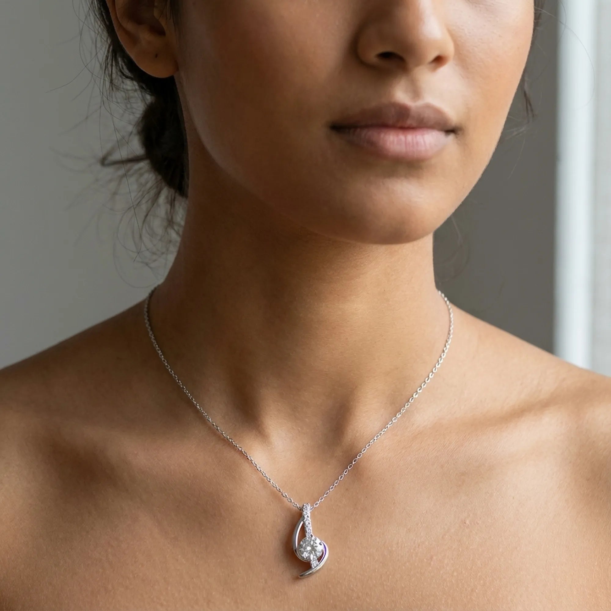 Woman wearing Swirl arc CZ pendant necklace at collarbone on fine silver cable chain, neutral background