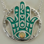 Close-up of a natural yellow opal bezel-set in a teal enamel Hamsa pendant showing its play-of-colour, 925 silver, Luna Dura.