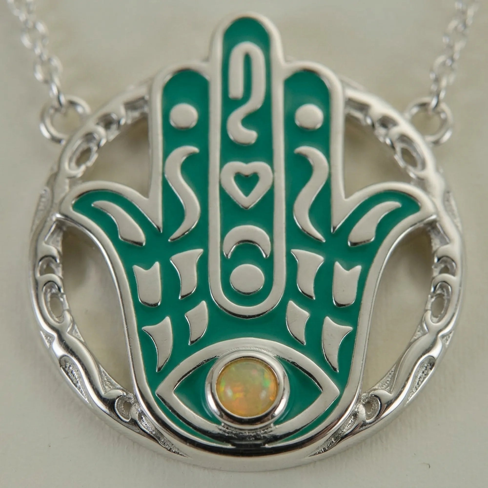 Close-up of a natural yellow opal bezel-set in a teal enamel Hamsa pendant showing its play-of-colour, 925 silver, Luna Dura.