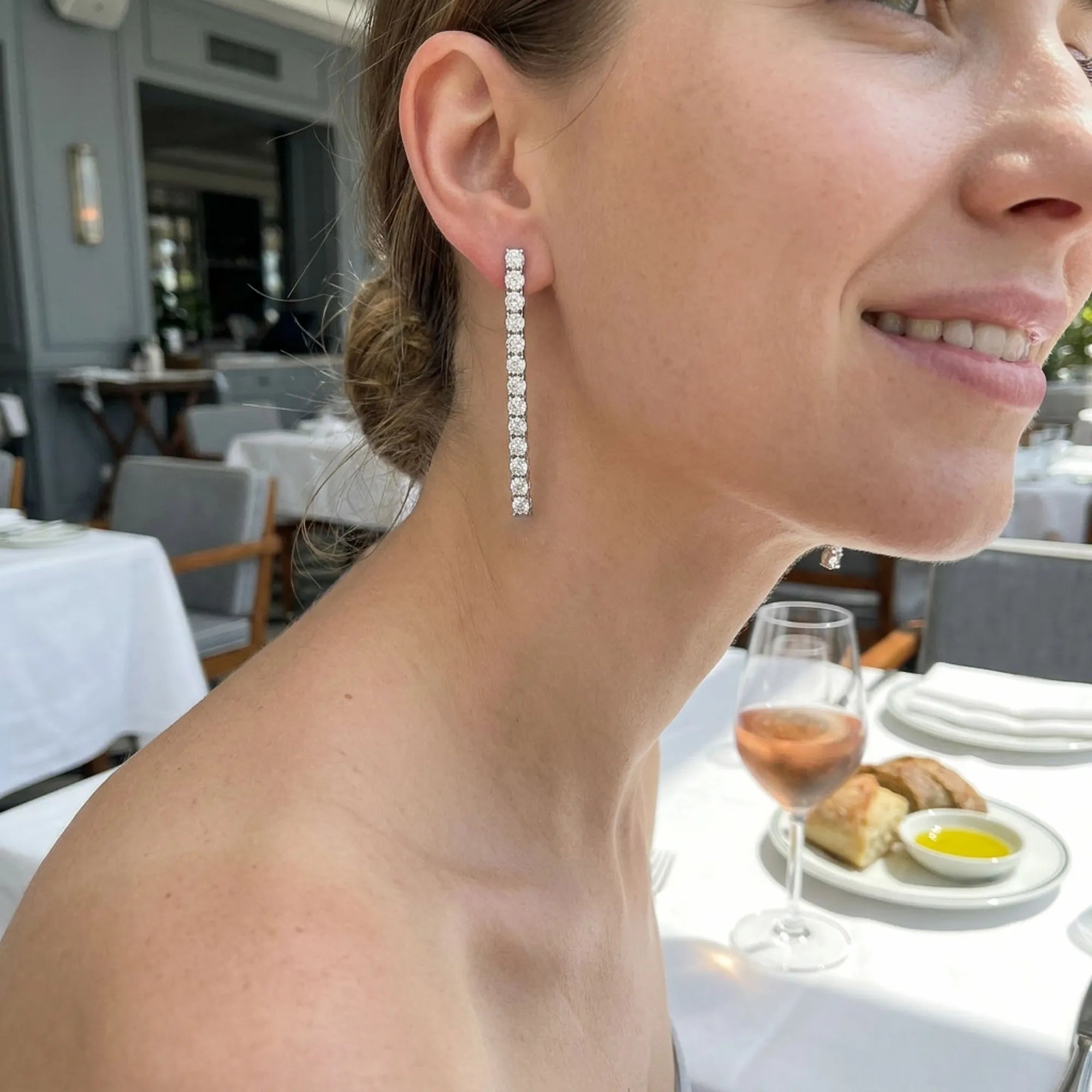 Model wearing CZ tennis drop earrings at La Petite Maison DIFC Dubai — 40mm stone line against neck at formal dinner setting