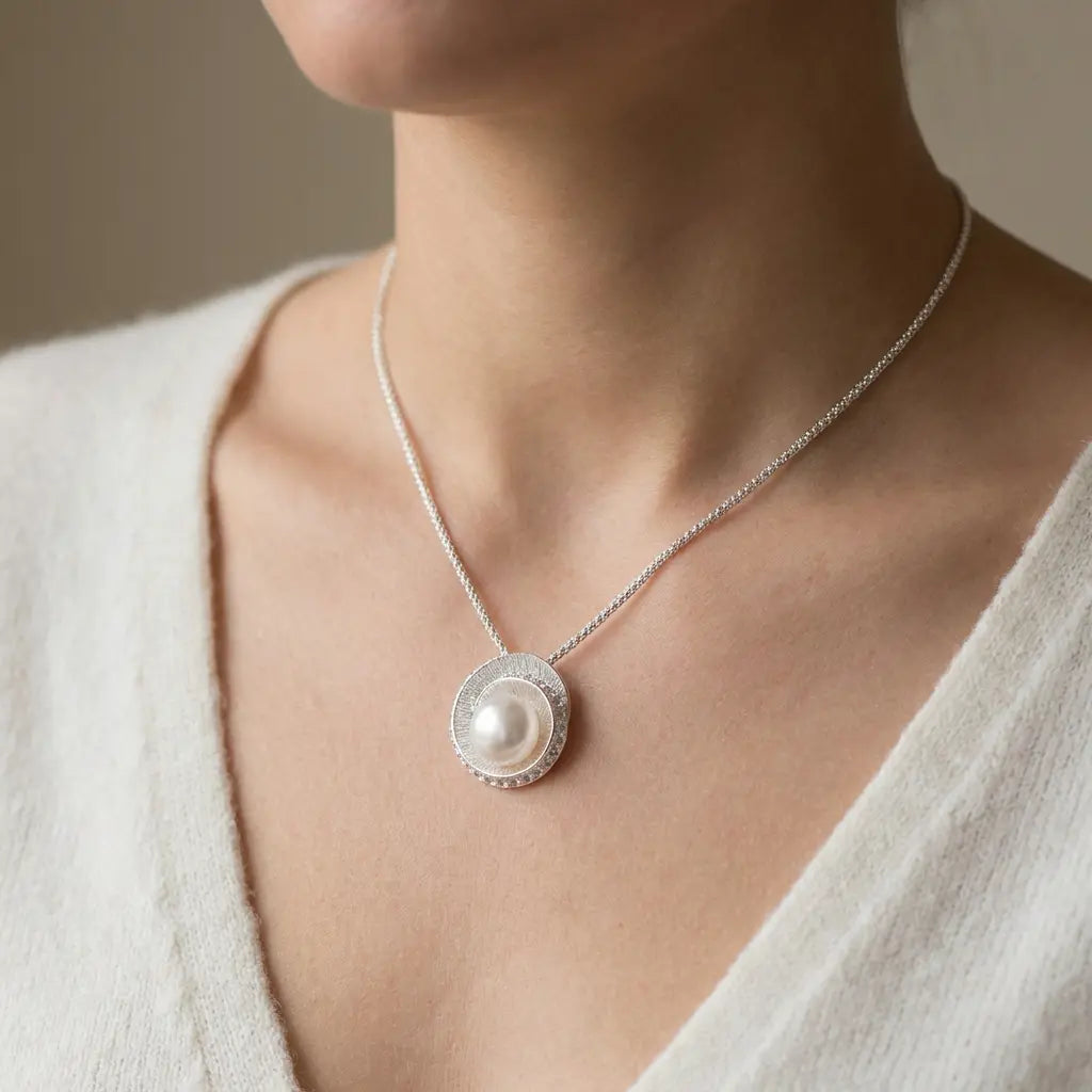 Model wearing a large round white pearl pendant set in a textured sterling silver swirl frame on a delicate silver chain
