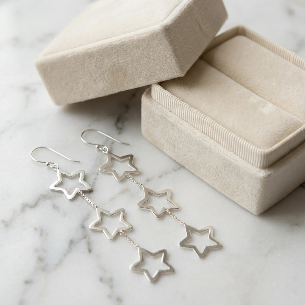 925 sterling silver triple star drop earrings beside an open cream velvet jewelry box on marble.