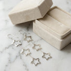 925 sterling silver triple star drop earrings beside an open cream velvet jewelry box on marble.