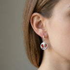 Close-up of red enamel tulip drop earring on ear showing circular disc and CZ-set ear wire