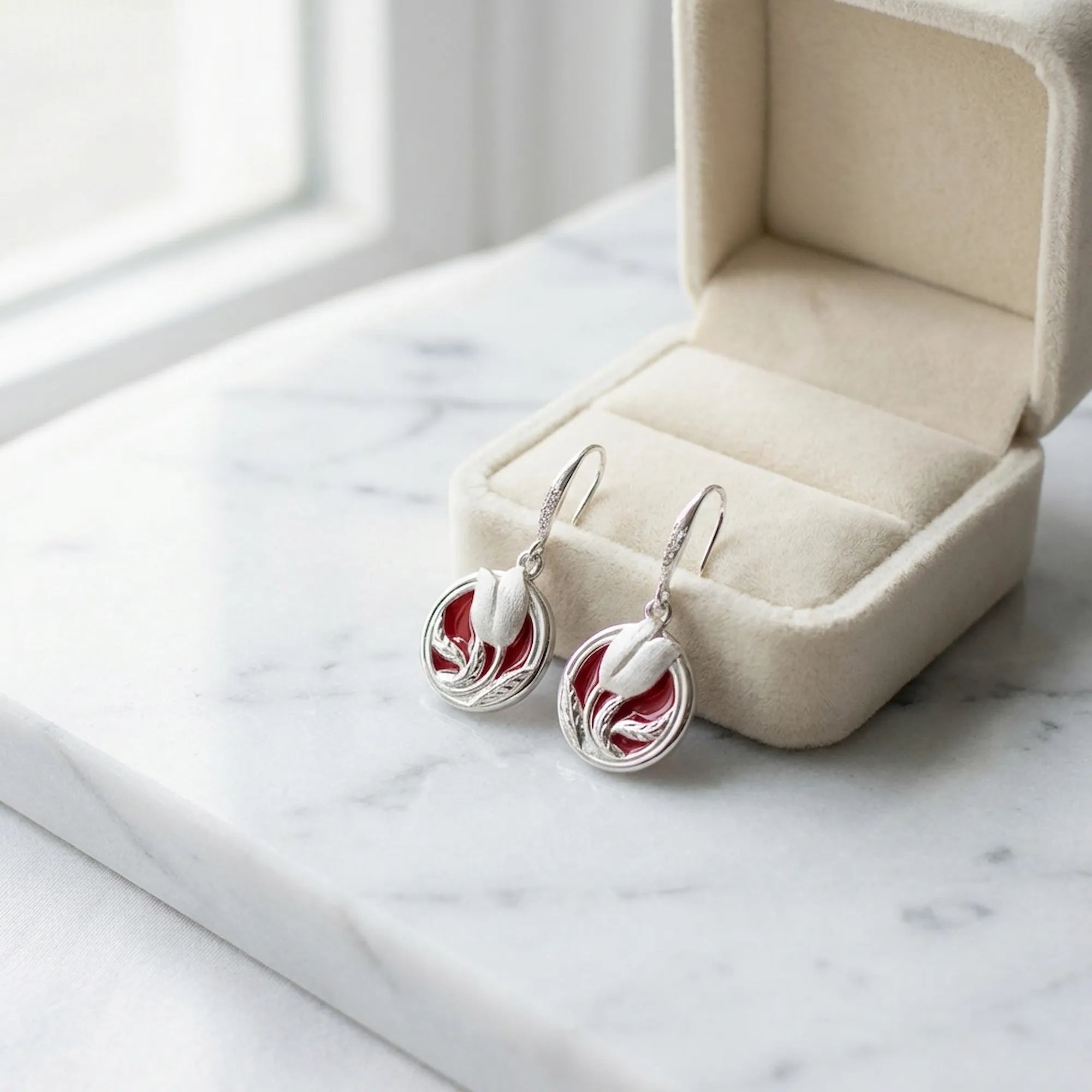 Red enamel tulip drop earrings in 925 sterling silver alongside open cream velvet jewelry box on marble