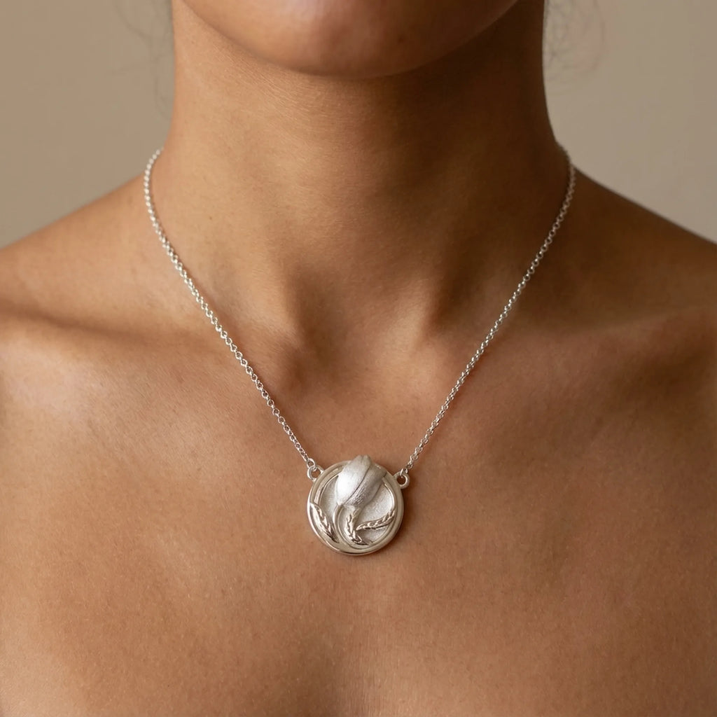 Close-up tulip medallion necklace on bare collarbone — satin silver bud in polished rim, 925 sterling silver