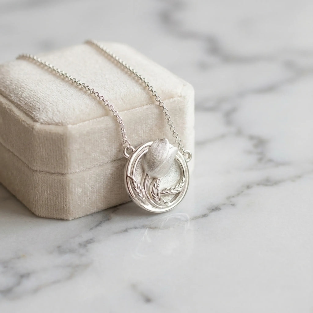 Tulip medallion necklace against cream velvet box on marble — 925 silver satin pendant, gifting flat lay