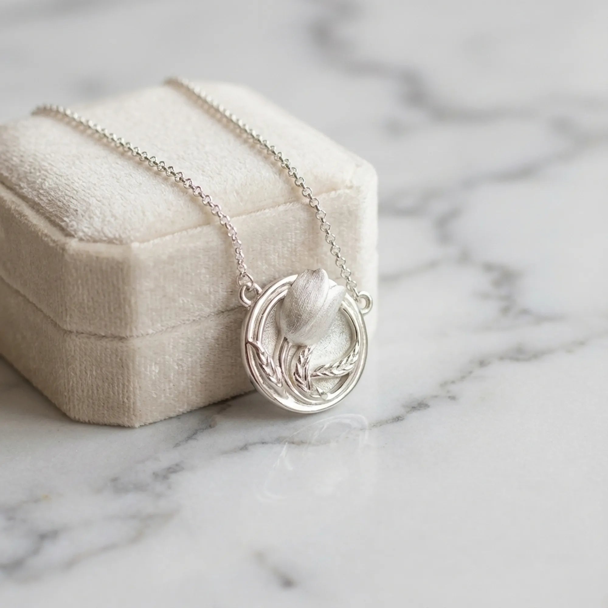 Tulip medallion necklace against cream velvet box on marble — 925 silver satin pendant, gifting flat lay
