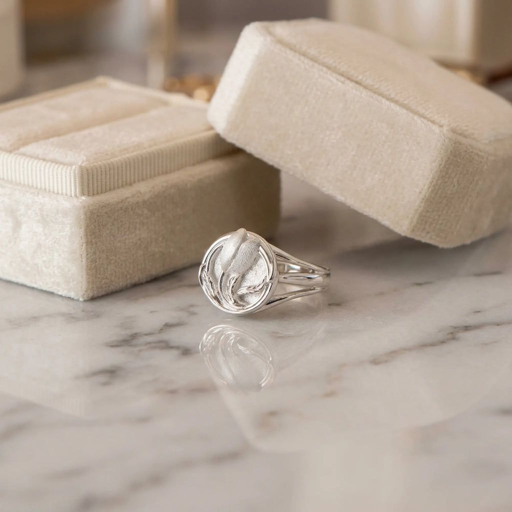 Satin silver tulip medallion ring on marble surface beside cream velvet jewelry box