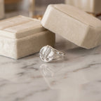 Satin silver tulip medallion ring on marble surface beside cream velvet jewelry box