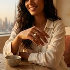 Satin silver tulip medallion ring on model hand with coffee cup and Dubai skyline through window