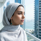 Turquoise heart drop earring worn by model with grey hijab — Dubai waterfront and skyscrapers in background