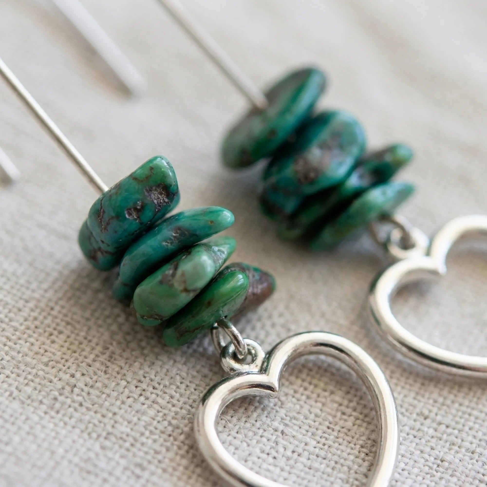 Close-up of raw turquoise chip stack and open heart silver charm — natural matrix veining visible on linen background