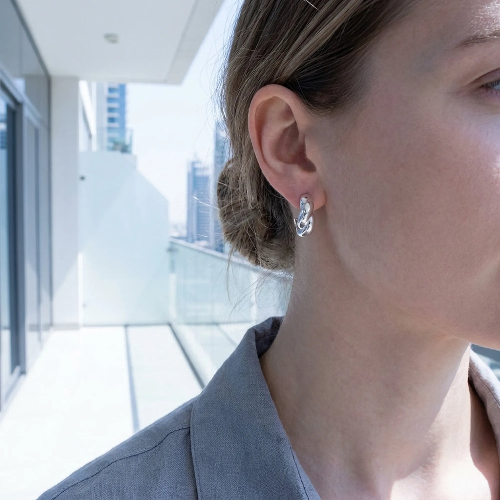 Sculptural twisted silver hoop earring worn on model's ear with Dubai skyline in background — 925 sterling silver