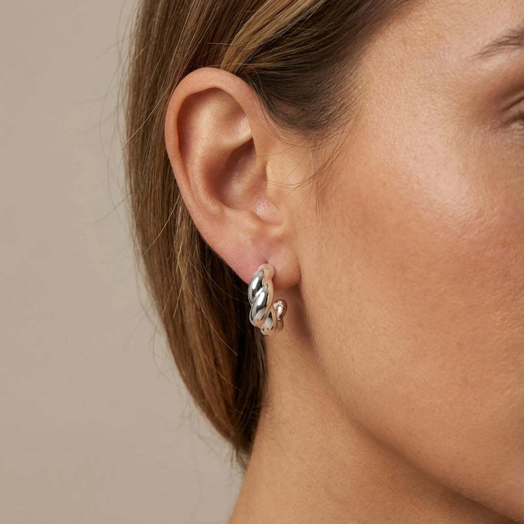High-polish twisted hoop earring worn close to earlobe — 15mm 925 sterling silver, neutral background