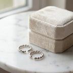 Pair of twisted rope oxidized silver ear cuffs on white marble surface beside closed Luna Dura cream velvet gift box