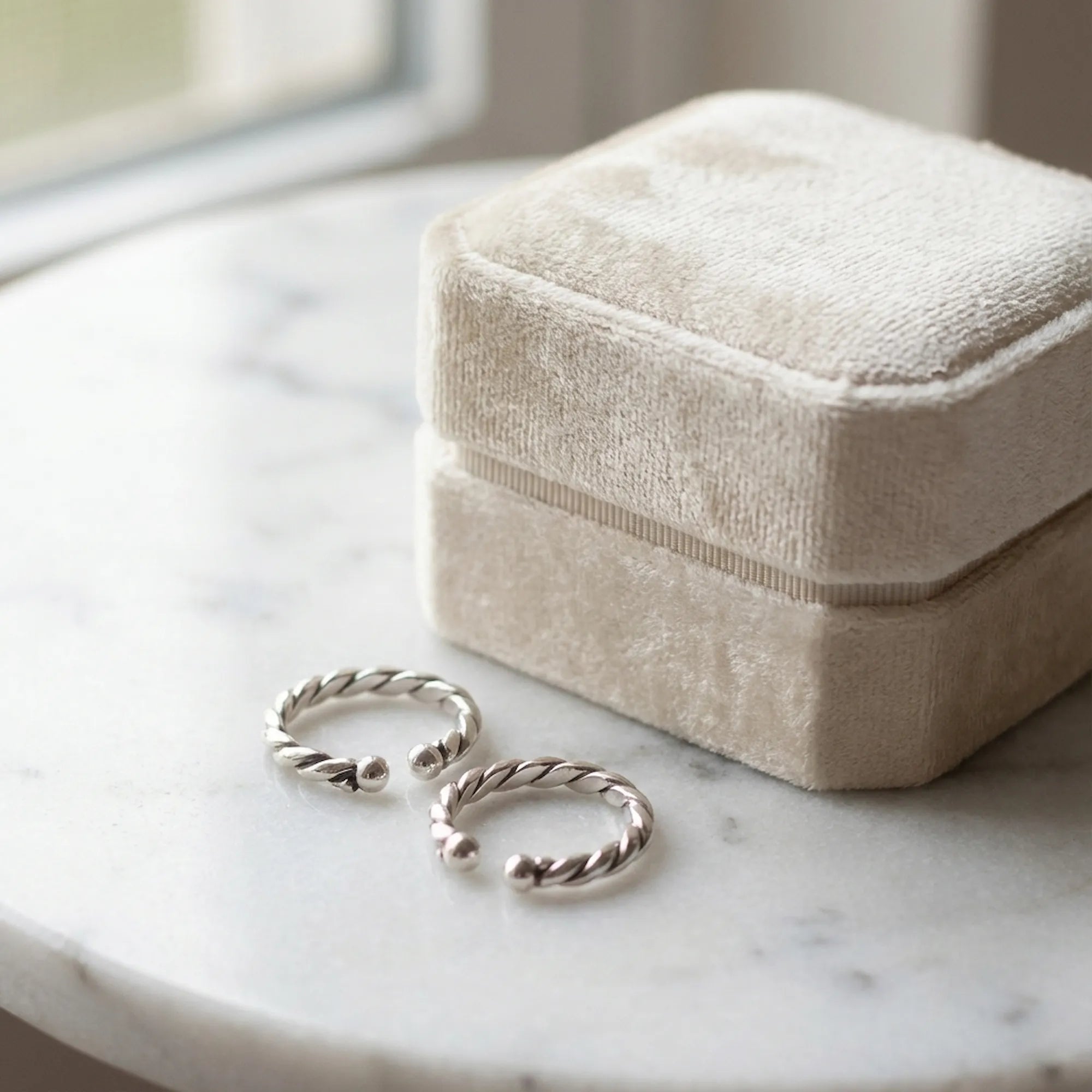 Pair of twisted rope oxidized silver ear cuffs on white marble surface beside closed Luna Dura cream velvet gift box