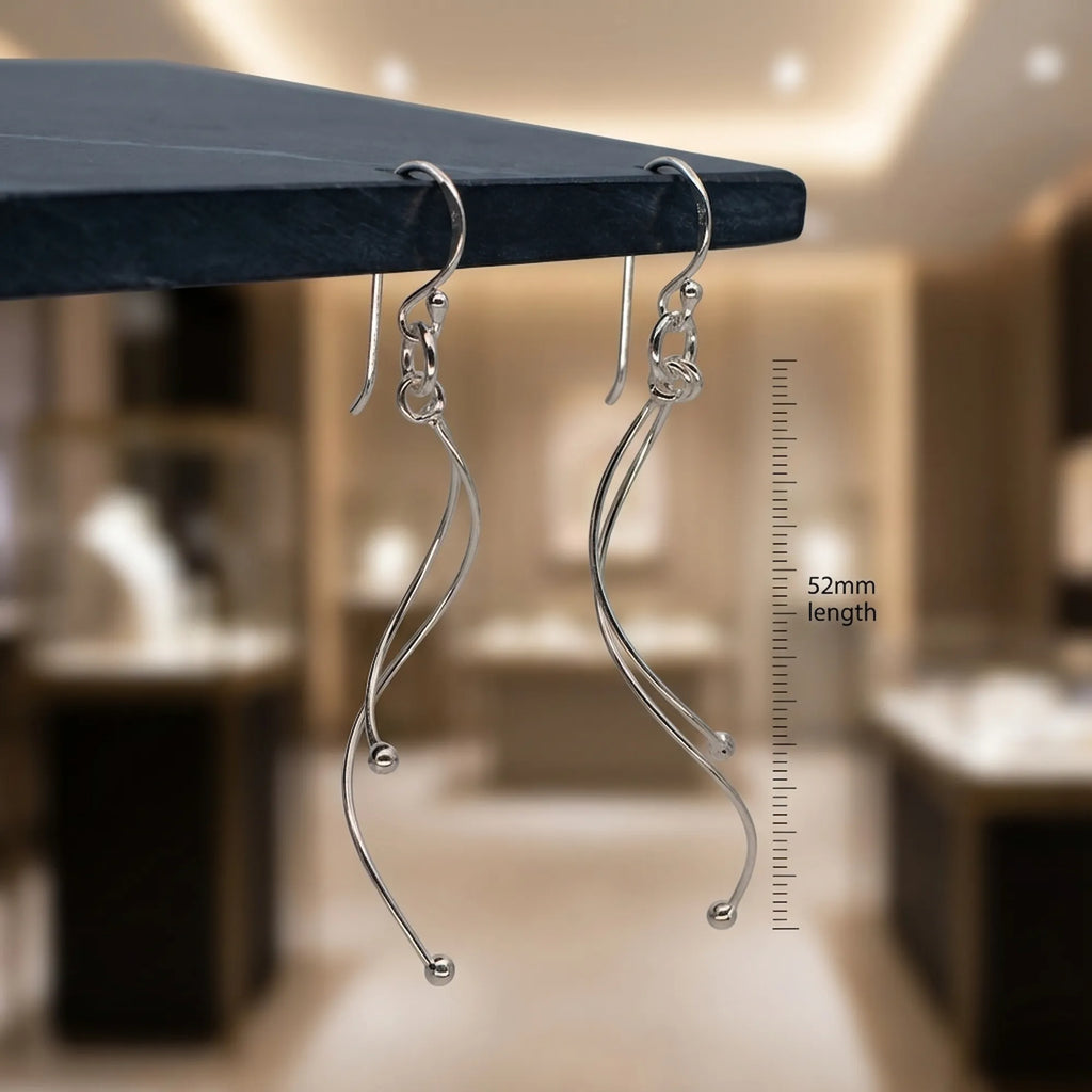 Silver wave drop earrings hanging on dark marble edge with 52mm ruler scale, jewellery boutique background