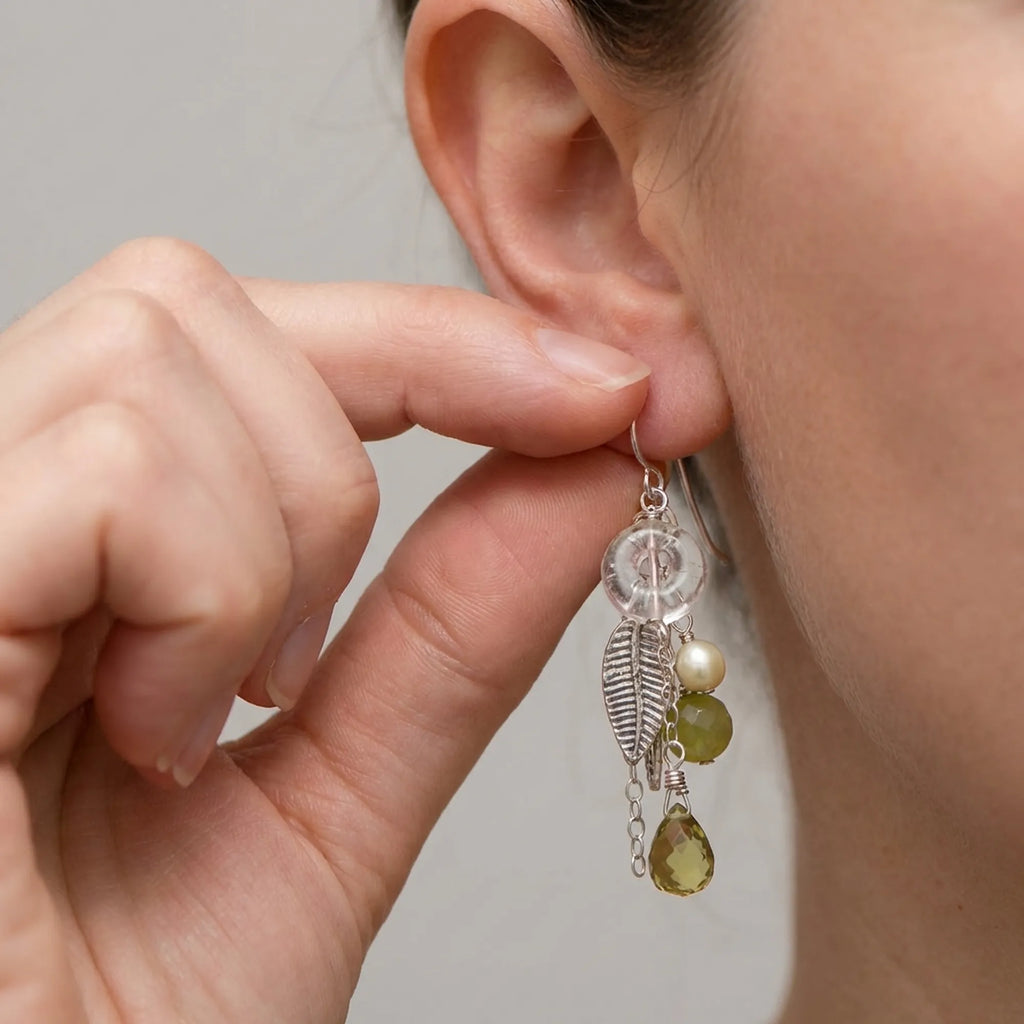 Easily securing the comfortable shepherd hook of our 925 sterling silver leaf chain drop earrings detailed with a lime green gemstone.